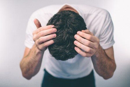 גבר רכון קדימה ומחזיק את הראש בשתי הידיים