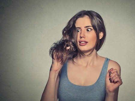 אישה צעירה מביטה בבהלה בקווצה מהשיער שלה